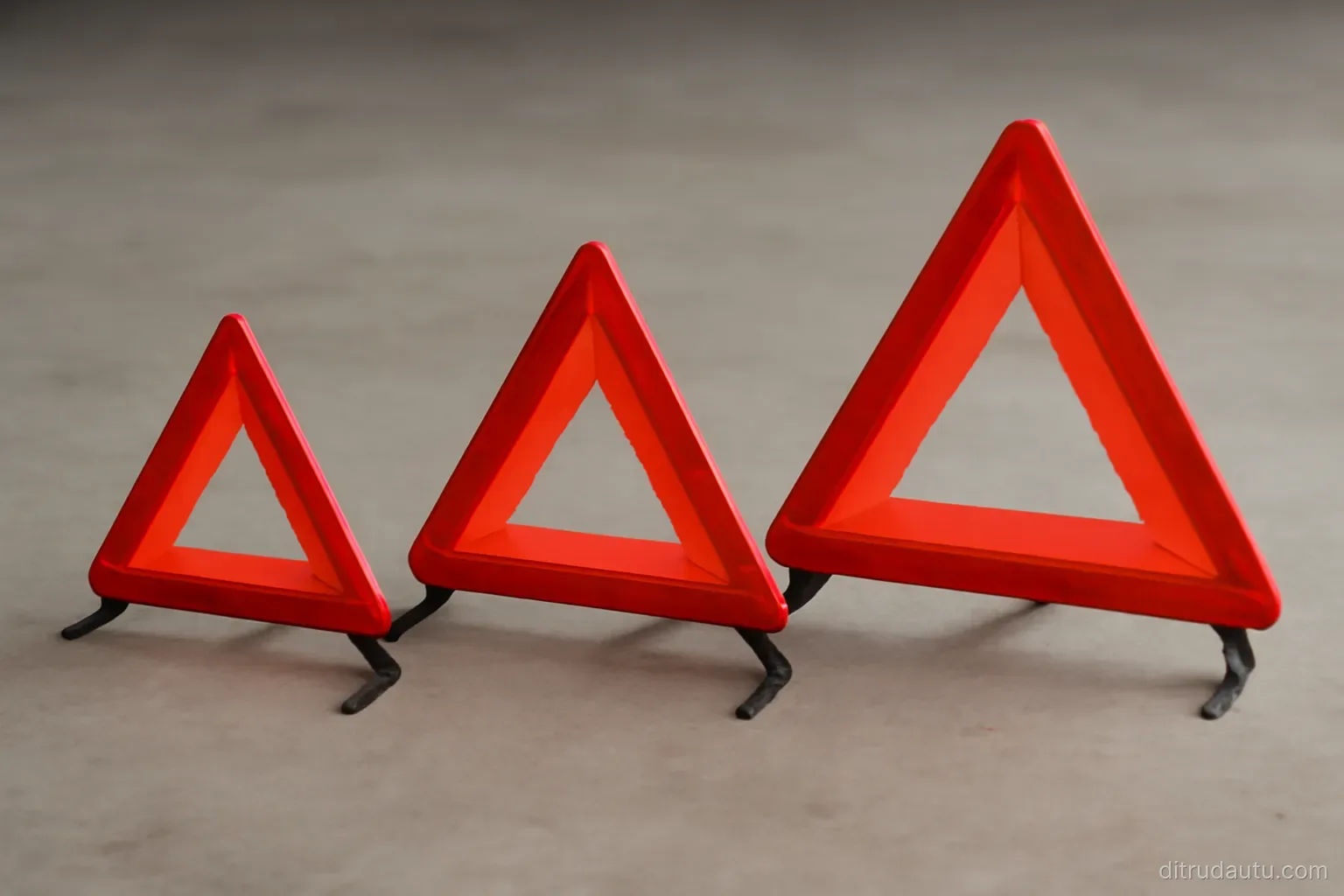 three plain warning triangles of different sizes standing in a row on a bare concrete floor under even lighting